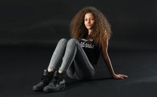 Portrait of the beautiful, sitting girl with curly hair, at black background