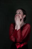 girl in a burgundy blouse closes her mouth with her hands