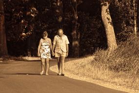 senior Woman and Man walking holding hands on path in park
