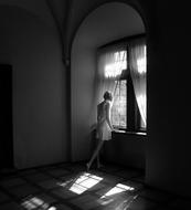Black and white photo with the girl, standing near the windows, in light