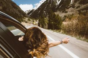 Woman, looking out of the window of the car, on the road, among the beautiful and colorful mountains, with the snow