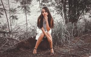 girl in a white dress sitting on a tree stump in the forest