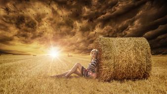 Woman Sitting on harvested field leaning to hay ball at sunset