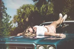 fashionable blonde lies on the hood of a vintage car