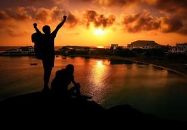 silhouette of two men on rock in front of water at sunset