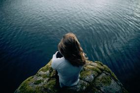 girl is sitting on a rock with green moss on the seashore