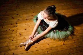 Ballerina girl in colorful clothing, sitting on the wooden floor in light