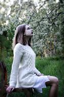 Lovely girl in white dress sits in blooming garden