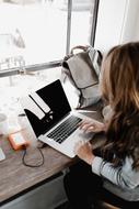 Woman using white and black laptop on the wooden table near the window