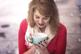 Smiling, blonde woman, with the beautiful, turquoise and white cup in the hands, among the snow, in the winter