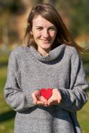 girl in a gray sweater with a red heart in her hand