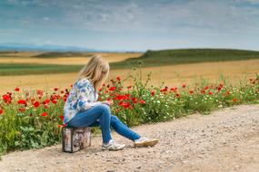 girl sitting on a suitcase on the road