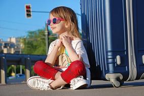 Girl is sitting near the blue suitcase
