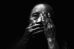 elderly woman closes her mouth and eyes with her hands