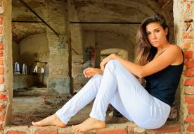 young Woman sits in window hole of ruined building