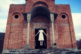 Woman in white, Halloween bride costume near the brick building with columns