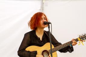 young redhead girl plays guitar at microphone