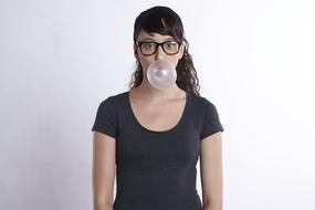 Portrait of the woman with glasses, making a bubble out of the bubblegum