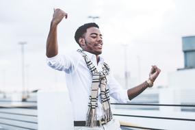 Afro American guy dancing in white shirt and pants by the fence