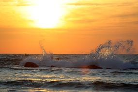 waves of the warm sea are hitting stones against the backdrop of a sunset in Greece