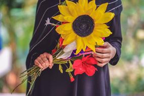 Close-up of the beautiful and colorful flowers in the hands of the bride, with the wedding ring, at blurred background with the colorful plants