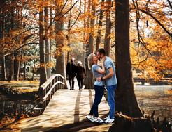 young couple kissing in park beneath Tree at fall