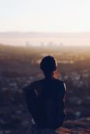 back view of girl sitting on rock above city