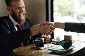 Agreement, Bearded mature man shaking hand with woman in cafe