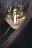 Portrait of the smiling woman, with the gold, shiny mask, among the darkness