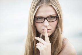 Blonde woman with glasses, holding finger on the mouth