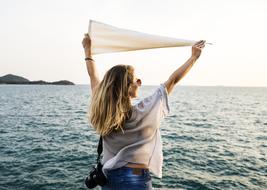 girl with white flag in hands above head at sea