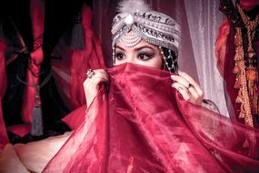 Eastern Girl with red veil at face among the colorful clothes