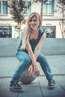 blonde sitting on a stone ball in the street