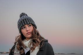 Portrait of a woman with gray hat and white scarf, at colorful sunset background in winter