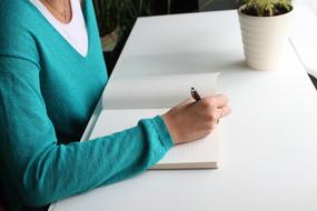 woman in Blue jumper Writing in the notebook at Desk