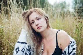 Blonde girl with long Hair and sad Eyes sitting on meadow