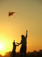 Mother and child son playing with kite at sunset