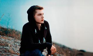 young man wearing black hoodie sits outdoor