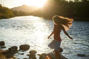 longhair young girl on riverside at Sunset