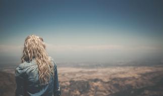 back view of Blonde Girl at blurred mountain landscape