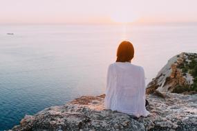 photo of a girl in a white sweater on a rock by the ocean
