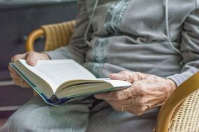 an elderly woman reading a book in a wicker chair