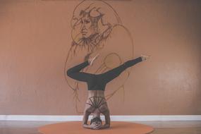 Woman doing yoga, with standing on the head, in the room with wall drawing