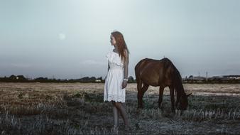 young Girl and grazing horse on harvested field at dusk