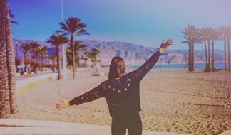 Back view of the girl, on the beautiful, sandy beach, with the colorful palm trees, near the mountains and water