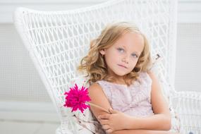 cute girl with a purple flower sits on a white armchair