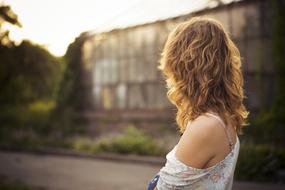 Back view of the young, blonde woman, looking on the building, among the colorful plants