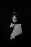 Black and white photo of the child girl, holding notebook, at black background