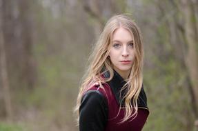 photo of a blonde in a jacket in the woods