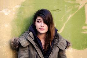 Portrait of the beautiful, smiling girl with colorful hair, leaning on the green and beige wall